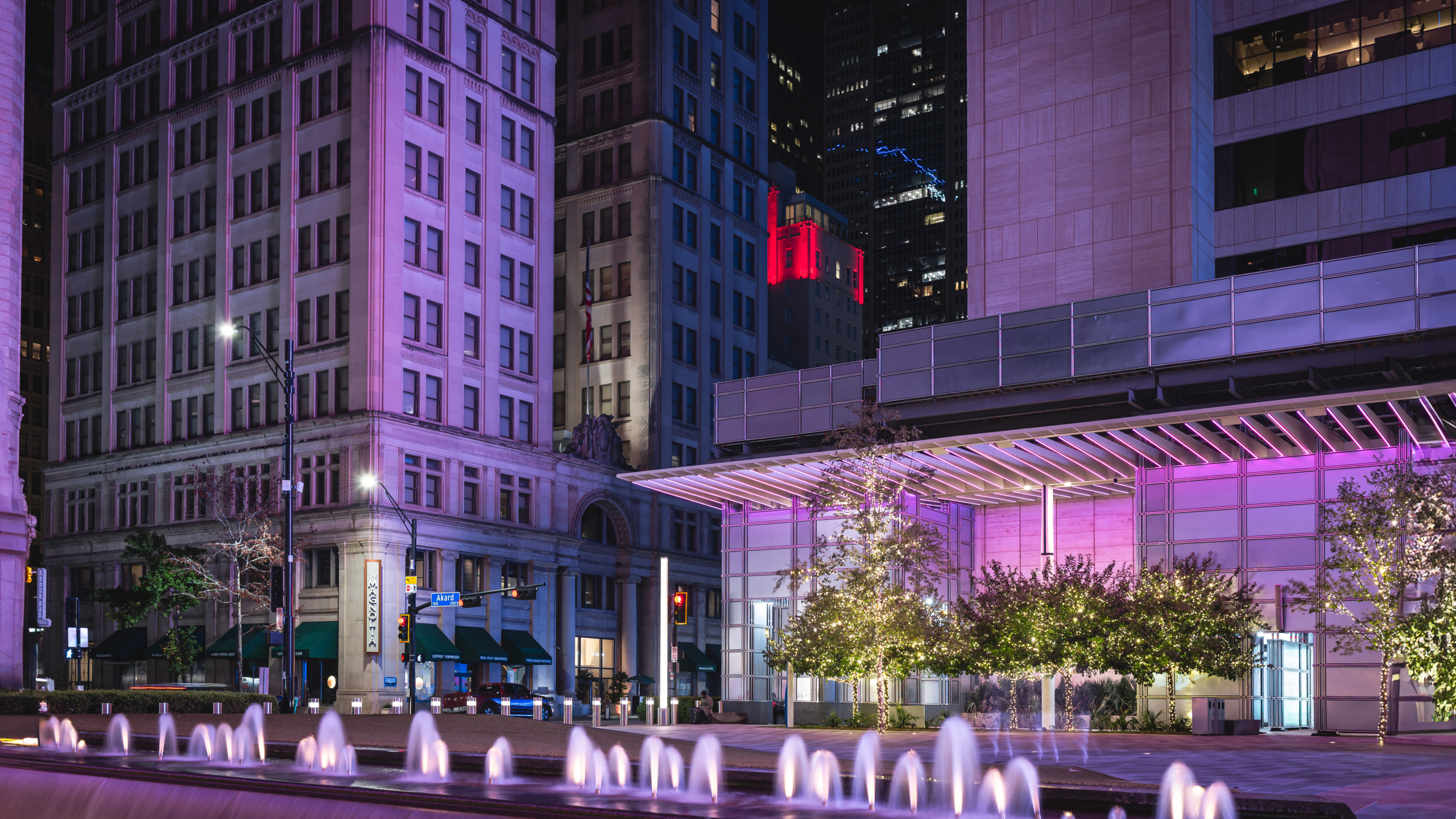 AT&T Plaza in downtown Dallas at night — fountain jets, a purple-lit modern pavilion, and historic limestone facades combine in a layered urban composition that proves Dallas saves its best look for after dark.
