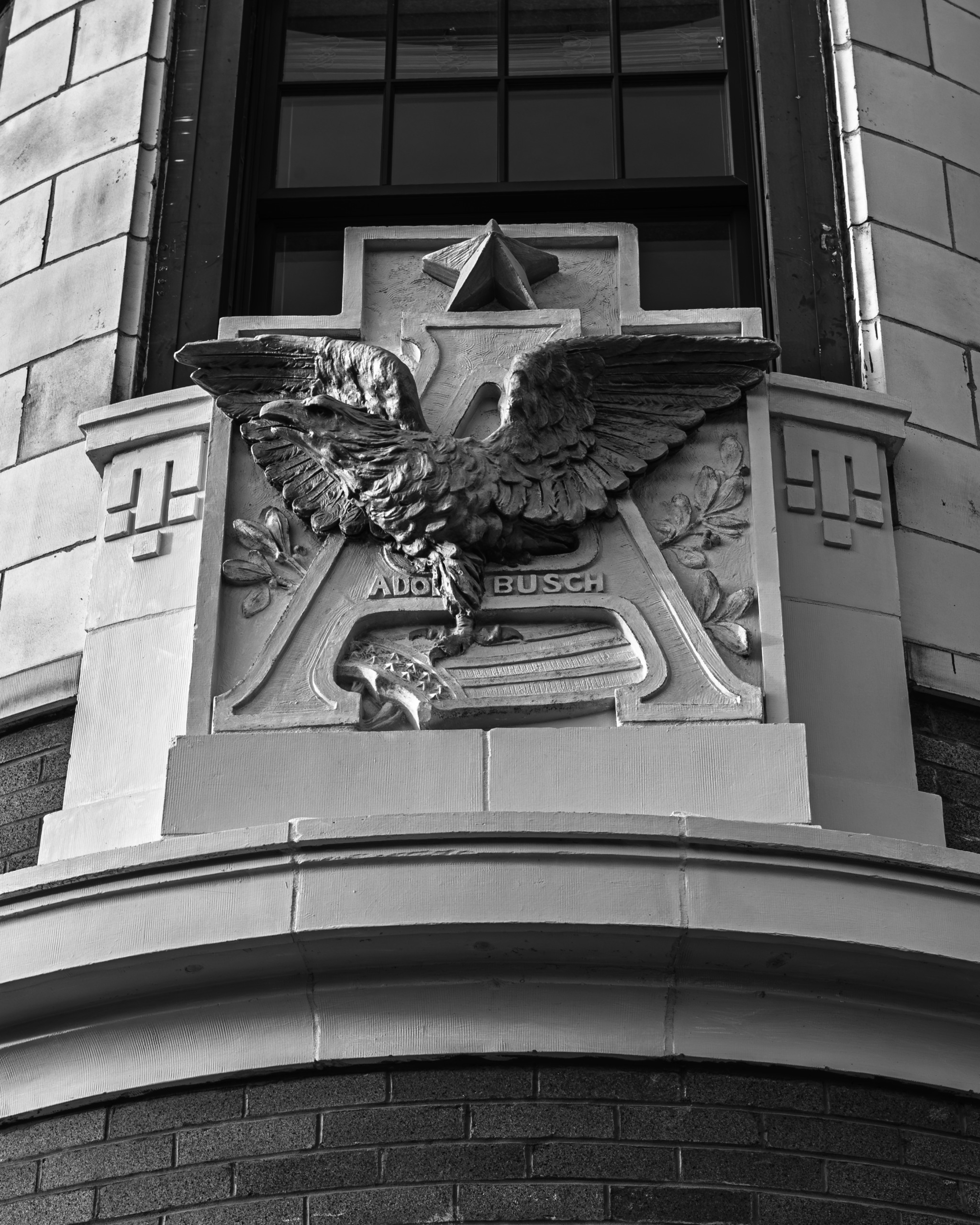 Black and white photograph of an ornate stone relief featuring the Anheuser-Busch eagle and Adolphus Busch name on the facade of a historic building in Peoria, Illinois.