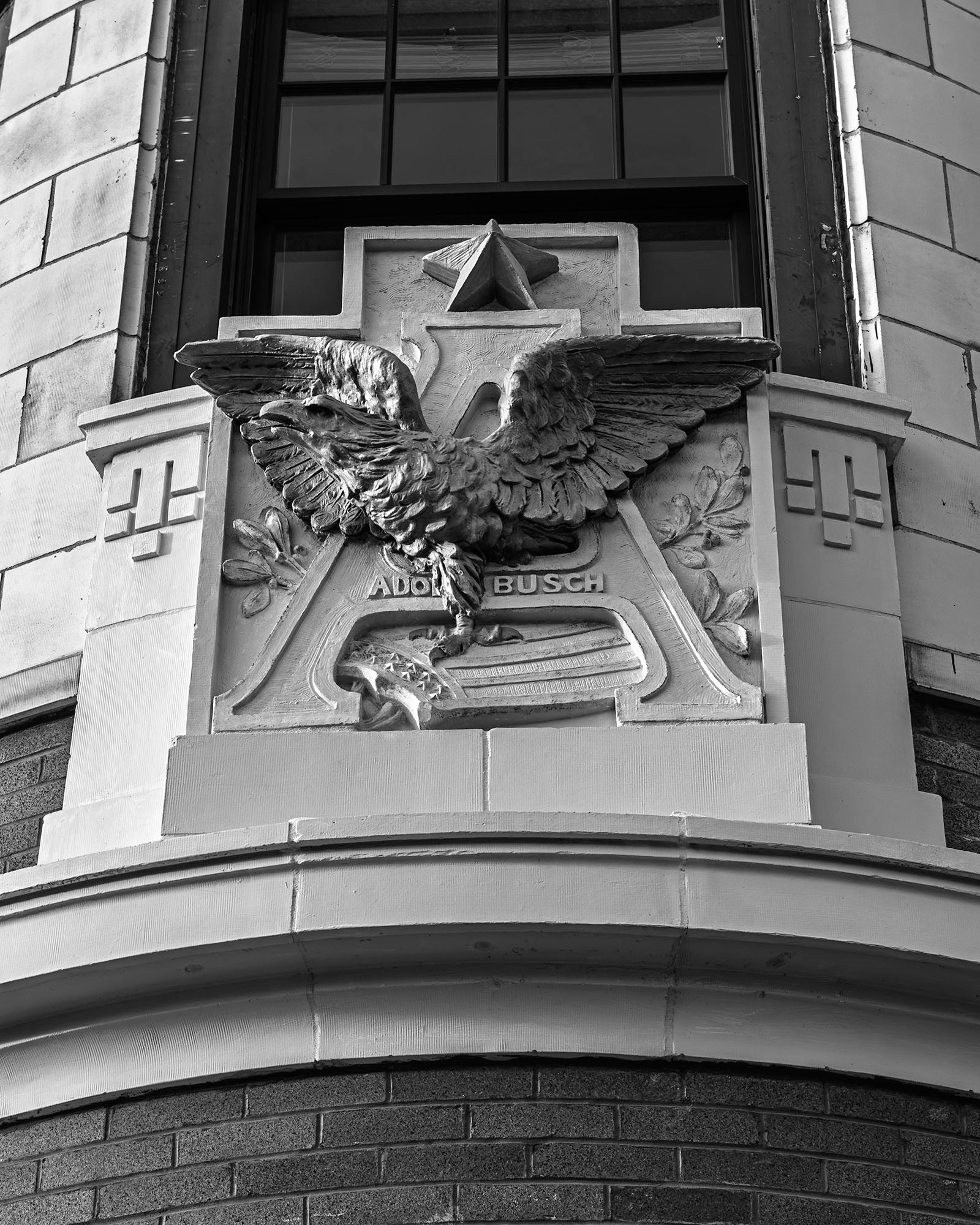 Black and white photograph of an ornate stone relief featuring the Anheuser-Busch eagle and Adolphus Busch name on the facade of a historic building in Peoria, Illinois.