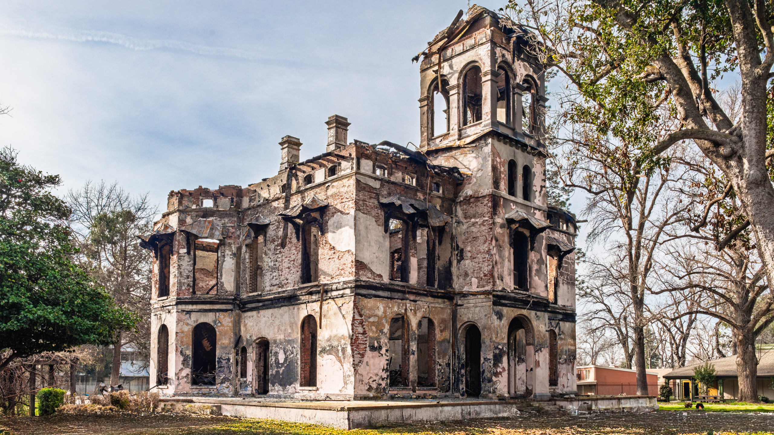 Fire-damaged ruins of the historic Bidwell Mansion in Chico, California, showing the surviving brick and plaster walls, arched windows, and Italianate tower against a winter sky following the December 2024 arson fire.