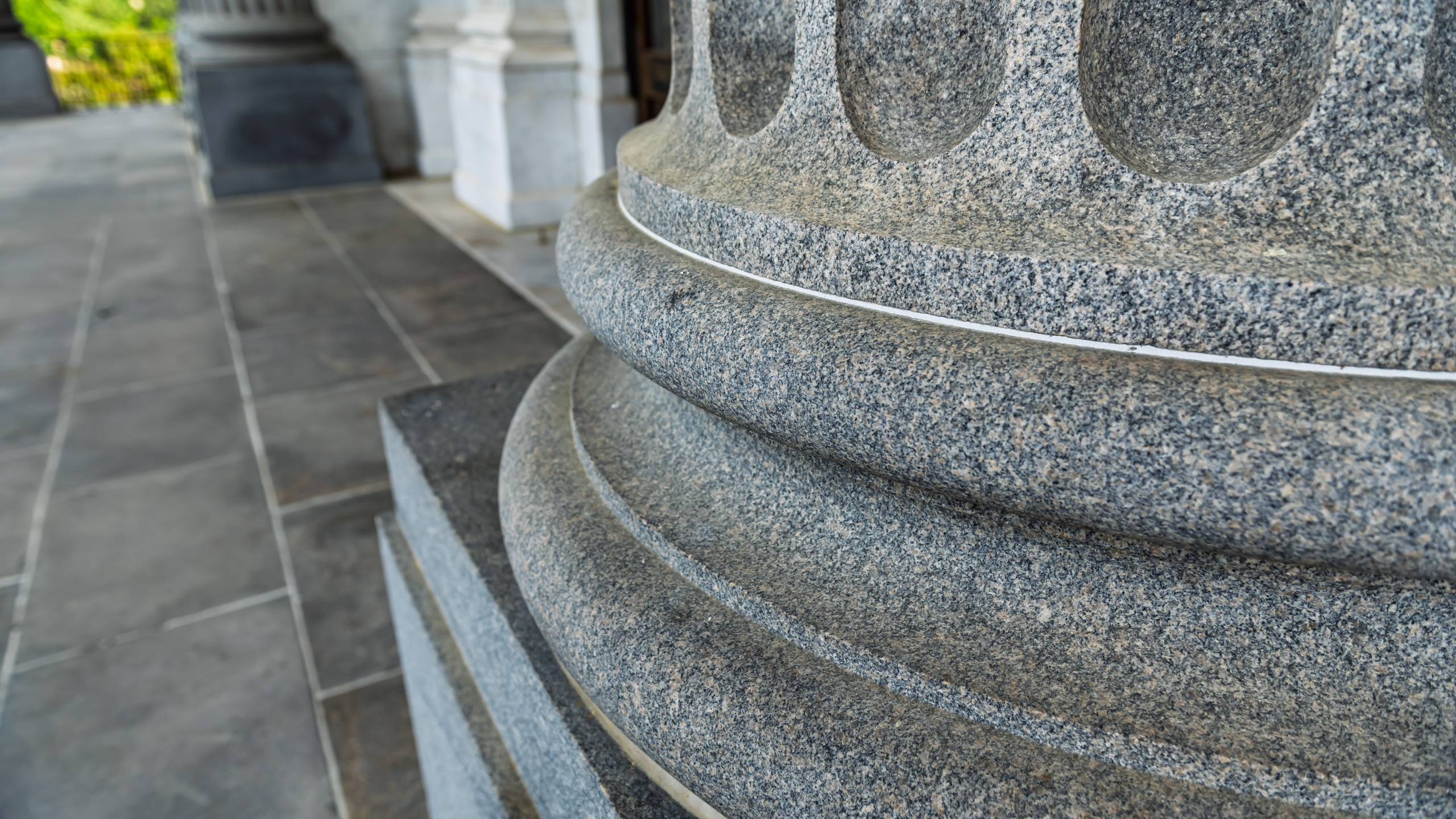 Close-up detail of a granite column base at the South Carolina State Capitol in Columbia, showing stacked torus moldings and the fine texture of gray speckled granite against a stone tile floor.