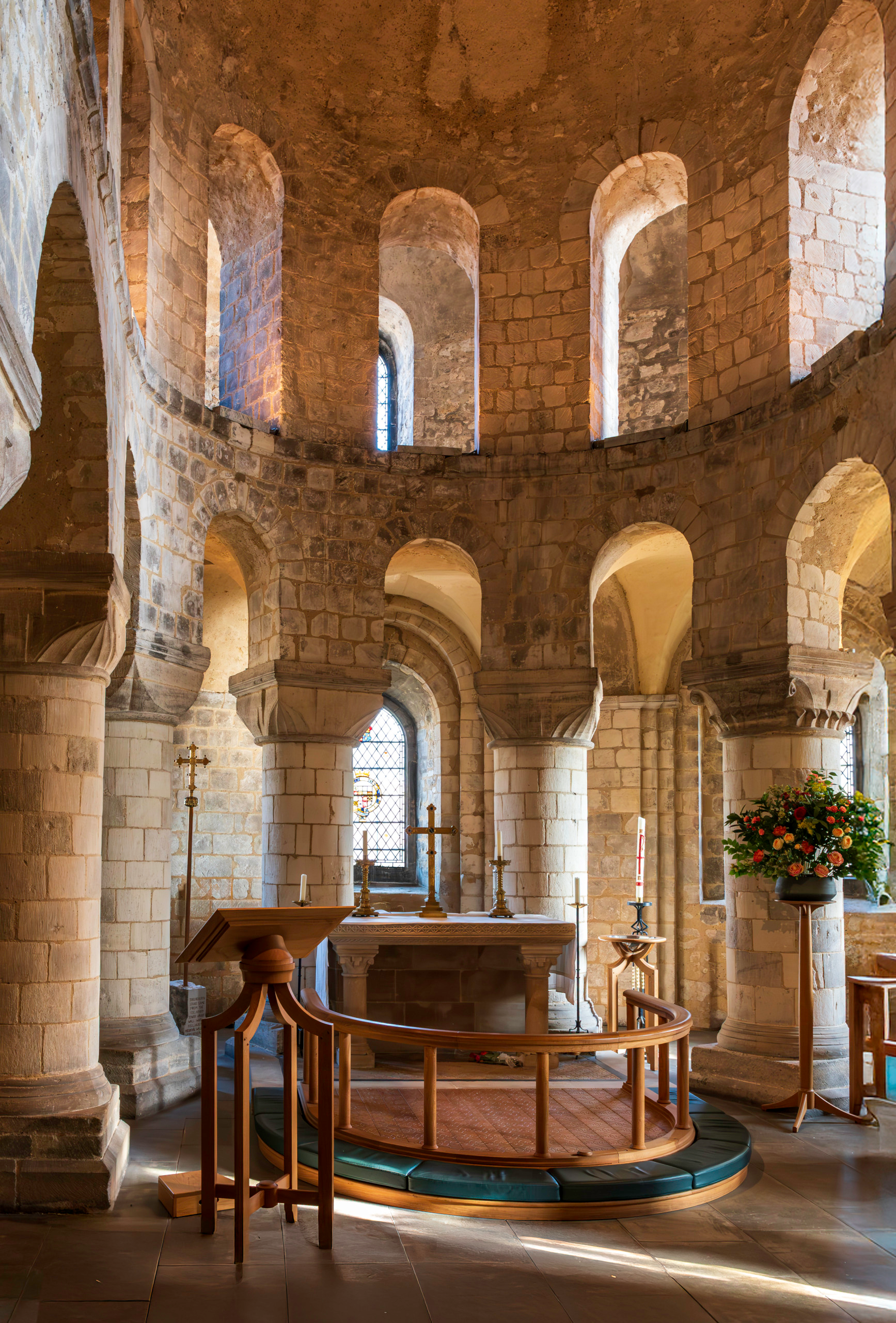 Interior of the Chapel of St. John the Evangelist inside the White Tower at the Tower of London, showing Norman stone arches, drum columns, and altar lit by natural window light.