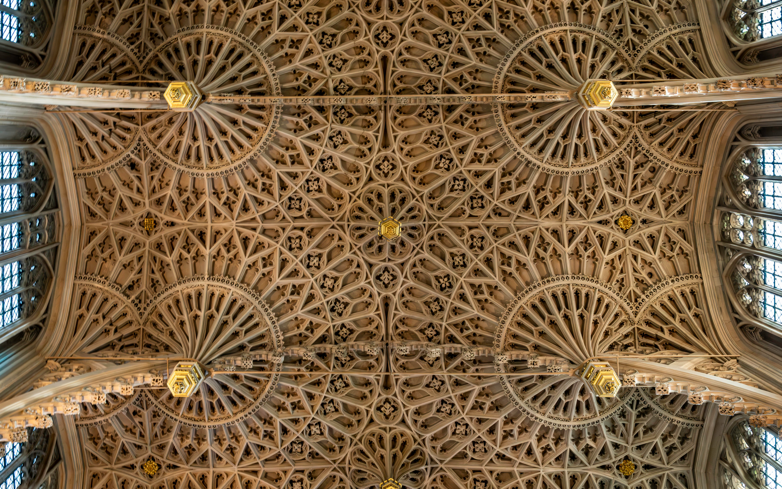 Looking straight up at the Gothic ribbed vaulting of Westminster Abbey's nave ceiling, featuring radiating stone ribs and ornate gilded bosses stretching the full length of the nave.