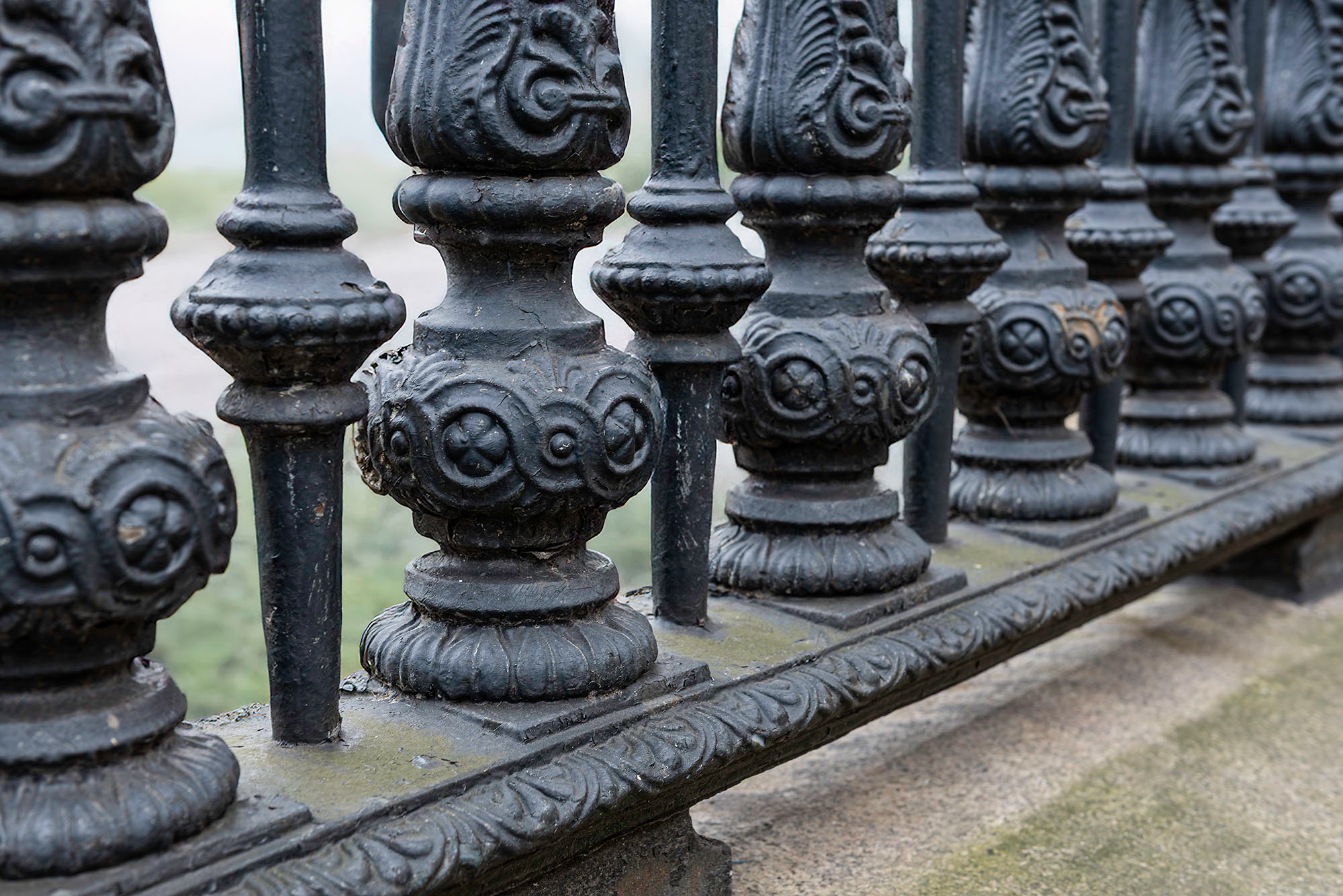 Close-up detail of the ornate Victorian cast iron perimeter fencing at the British Museum in London, showing decorative balusters with acanthus leaf caps, medallion-studded mid-sections, and layered base moldings on a overcast day.